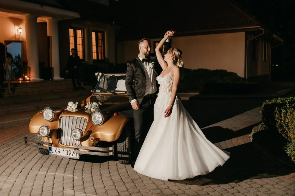 Para młoda pozuje przy złotym samochodzie na weselu