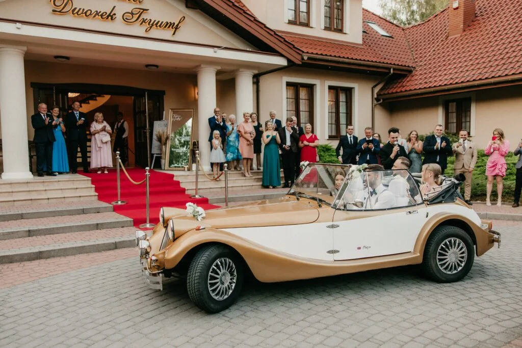 Młoda para wjeżdża na wesele zabytkowym kabrioletem przed Dworek Tryumf