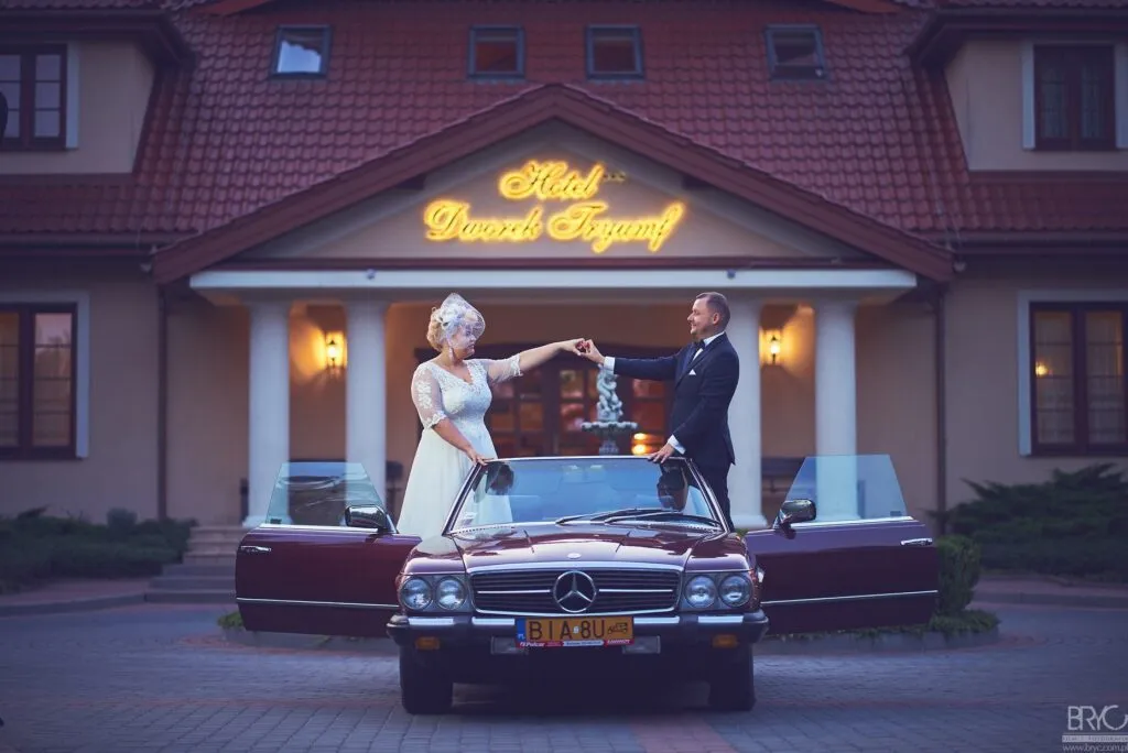 Para młoda przy zabytkowym kabriolecie przed wejściem do Hotelu Dworek Tryumf.