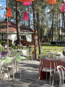 Taras restauracji Dworek Tryumf z białymi stołami i krzesłami, ozdobiony kolorowymi lampionami.