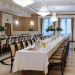 Elegancka sala weselna w Dworku z długim stołem i kryształowymi żyrandolami.